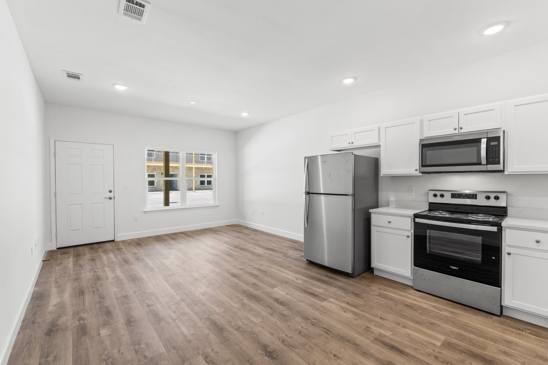 Finished apartment kitchen with white shaker cabinets, stainless appliances, and LVP flooring in a new multifamily building by Whitrock Associates, Northwest Florida