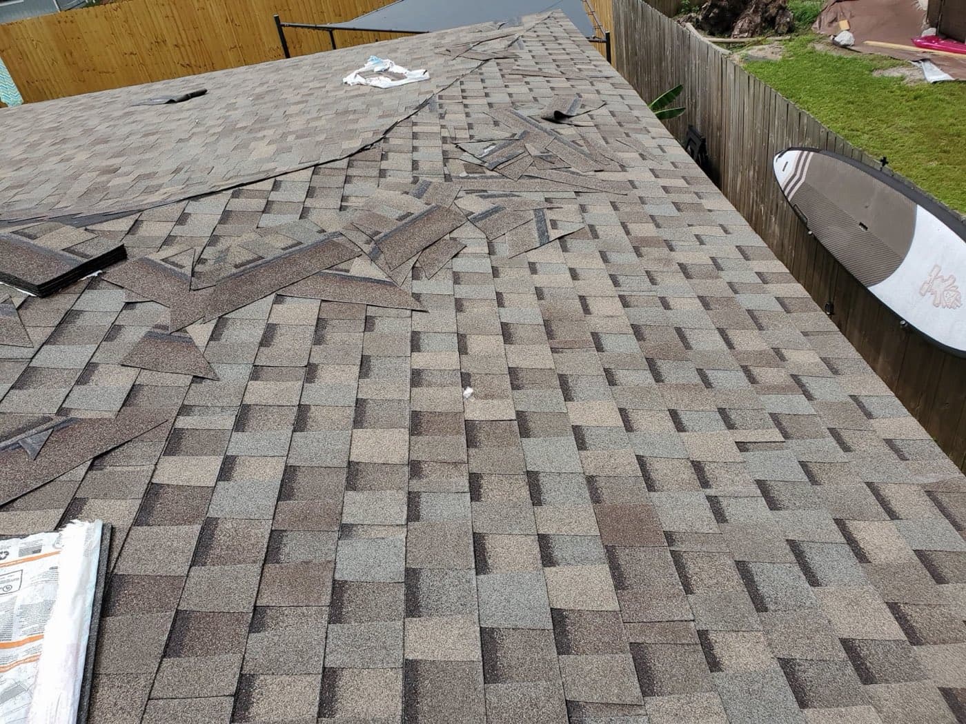 Hurricane-damaged roof with lifted and torn shingles in Northwest Florida